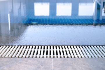 Overflow swimming pool grill closeup with a reflection on surface of clear water 