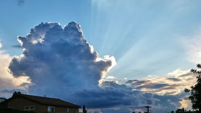 White clouds rolling in the sky and blocking the sun, houses and trees below. time-lapse