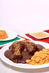 Mexican mole with sesame seeds on top accompanied by red rice, on one side green, white and red napkins. Copy space for advertising.