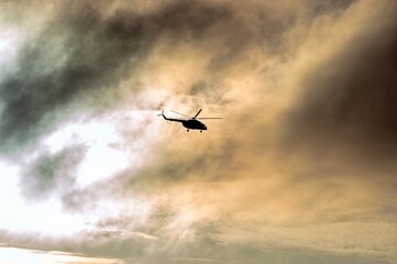 A helicopter is flying in the clouds illuminated by the sun