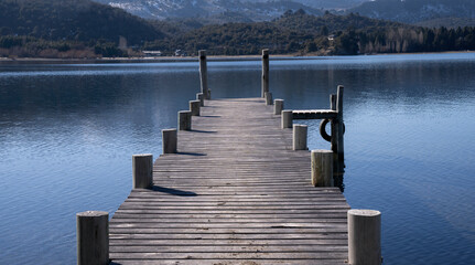 Naklejka premium The wooden docks into the placid lake. View of the blue sky, forest and mountains reflection in the water. 
