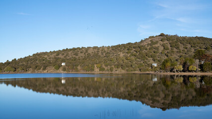 Symmetry in nature. Panorama view of the calm lake. The hills, green forest and clear blue sky...