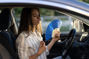Exhausted young woman driver with hand fan suffering from heat in car, has problem with a...