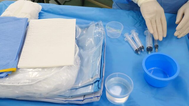 Preparation for vascular surgery in modern clinic. Professional doctors in surgical gowns and gloves preparing stuff to remove thrombus from artery in hospital. Using contrast liquid for examination