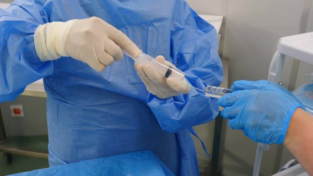 Preparation for vascular surgery in modern clinic. Professional doctors in surgical gowns and gloves preparing stuff to remove thrombus from artery in hospital. Using contrast liquid for examination