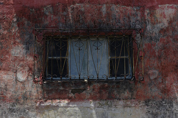Red cement wall texture with a rusty iron window,