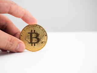 Closeup finger holding golden bitcoin on the table white background copy space