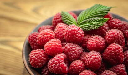 Bowl with fresh ripe delicious raspberries and a green leaf on a wooden background