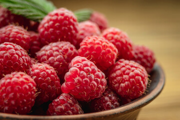 Bowl with fresh ripe delicious raspberries and a green leaf on a wooden background. Closeup