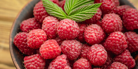 Bowl with fresh ripe delicious raspberries and a green leaf on a wooden table