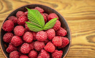 Bowl with fresh ripe tasty raspberries and a green leaf on a wooden background. Top view