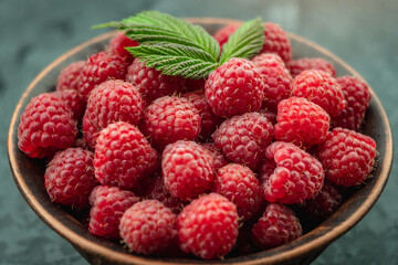 Bowl with fresh ripe delicious raspberries and a green leaves on a black background