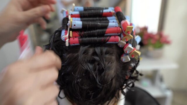 Close-up of a woman from behind with curlers on her hair while a perm, the master removes the curlers from her hair.