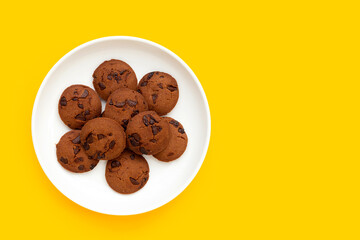 Chocolate chip cookies in white plate on yellow background.