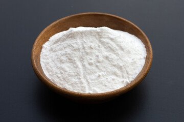 Baking soda in wooden bowl on dark background.