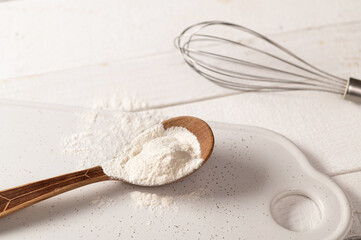 xanthan gum food additive for dough on white plate in wooden spoon with metal whisk