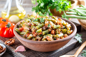 Green beans with vegetables and tomatoes. Food cooking background, vintage wooden table.