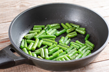 Green string beans in a frying pan on a wooden background.