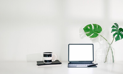 Blank screen tablet with keyboard on the table in white room background.