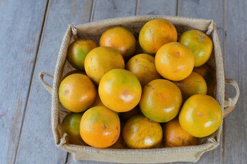 An organic mandarin or tangerine is placed in a rectangular burlap basket on a wooden table. Oranges are sweet and sour fruit that are high in vitamin C and fiber.It commonly used to make fruit juice
