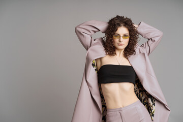 Studio shot of pretty fashion model in pastel purple leather trousers, coat, khaki sunglasses on...