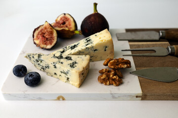 Blue cheese Forme D`ambert on a cheese board with figs, walnut and blueberry on white background