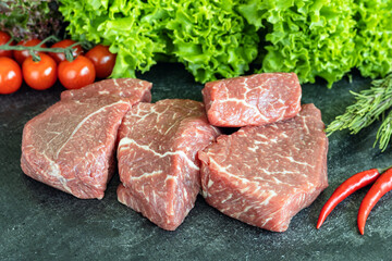 Raw fresh marbled beef meat and fresh salad leaves on dark stone cutting board