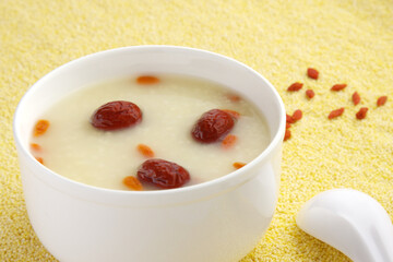 Red date wolfberry millet congee in a white bowl placed on a surface paved with millet rice, healthy and wholesome