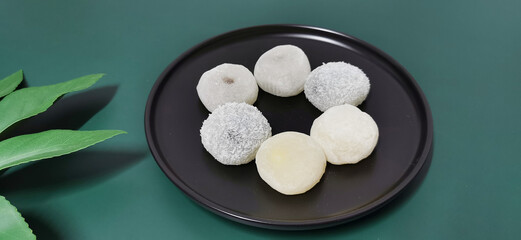A few different flavored glutinous rice balls arranged in a circle on a black, round plate, dark green background