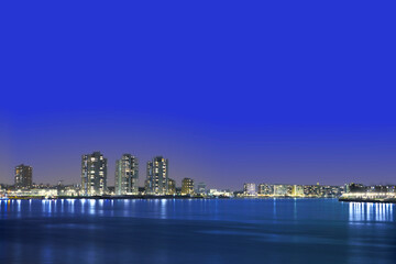 Fototapeta na wymiar The night view of a coastal city under the blue sky. The entire city is lit.