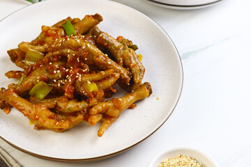 Korean Spicy Chicken feet or ceker ayam saus Gochujang served on white plate with sesame seed and slices onion spring. Bright mood food photography.