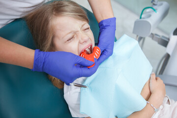 Little girl crying in dental chair while dentist making dental impressions with putty