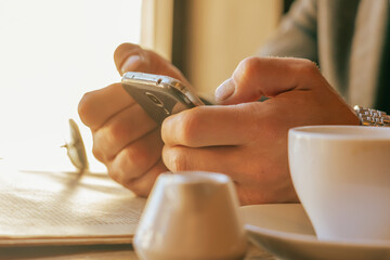 Conceptual image: world through smartphone, the reality of virtual life. Adult man monitors important events using the digital device and drinking coffee in a cafe.