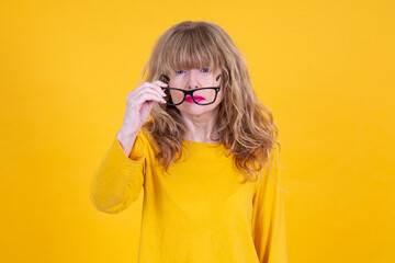 Woman has vision problems, squints her eyes while trying to see something, takes off her glasses, isolated on yellow background. Myopia, hyperopia, vision concept. See Less