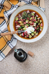 Plate of traditional russian cold soup with kvass or okroshka, flatlay on a beige marble...