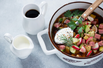 Close-up of okroshka or russian cold soup with kvass in a white serving pan, studio shot on a light-blue stone background