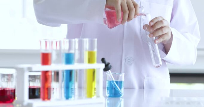 Young little primary schoolboy wearing doctor gowns dress trying to mix the colorful liquid solution and watch the result with concentrate and focus.  Concept of schoolboy learning and studying.
