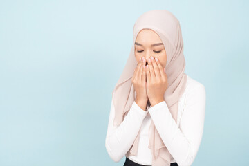 A beautiful young Muslim girl in hijab head scarf praying isolated on blue background.
