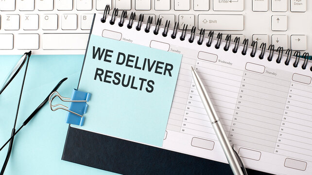 WE DELIVER RESULTS text on blue sticker on the planning and keyboard,blue background