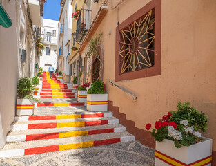 Fototapeta na wymiar Calle Puchalt is a bright and narrow alley in the center of Calpe with the staircase painted in the colors of the Spanish flag.Costa Blanca, Spain