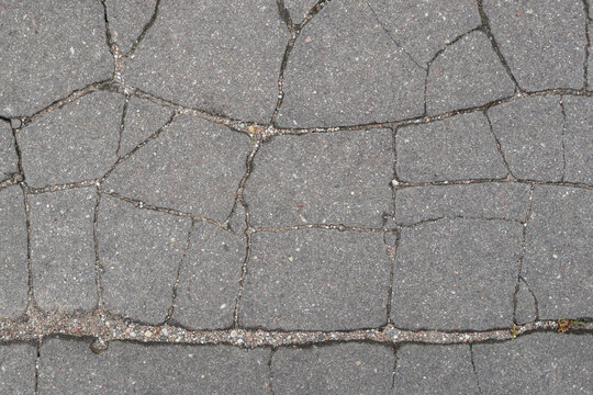 An old asphalt road surface with a surface torn by chaotic narrow cracks and wrinkles filled with small pebbles. Vintage, grunge abstract design background.