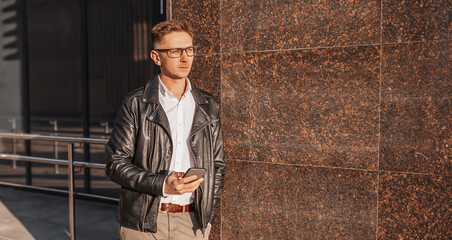 Handsome man with glasses with a smartphone on the street of a big city. Businessman talking on the phone on urban background