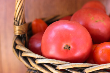Ripe juicy red tomatoes in a wicker wooden brown basket close up. Bio vegetables
