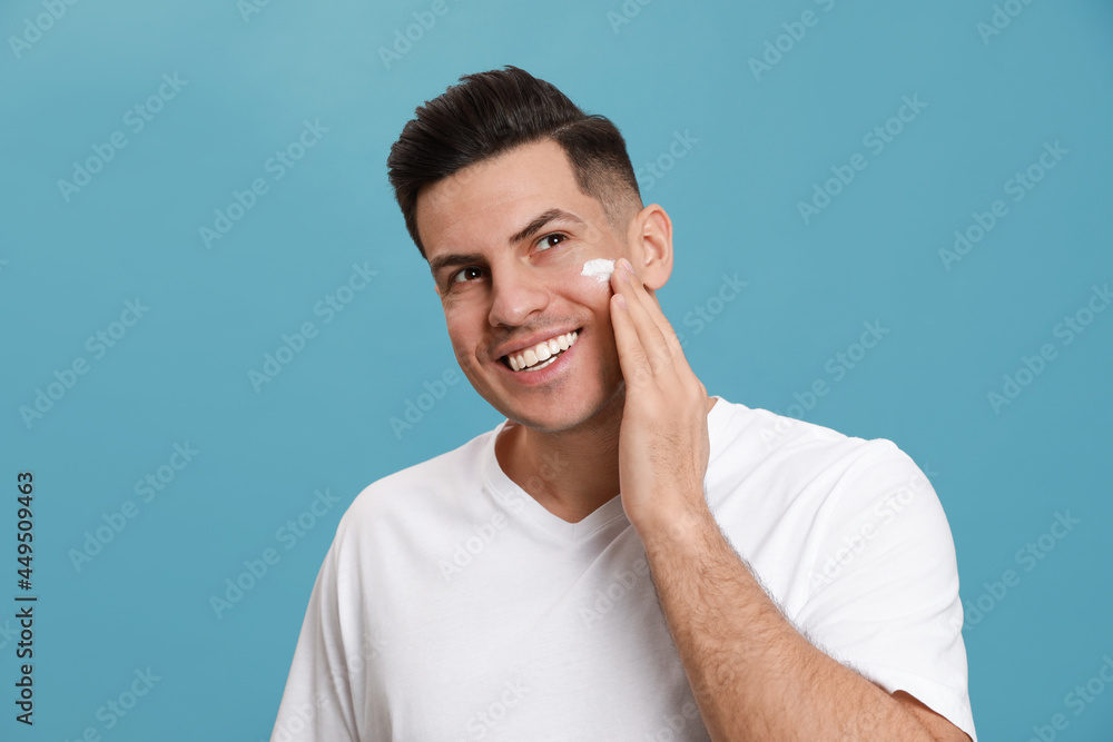 Poster happy handsome man applying face cream against turquoise background