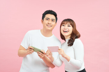 cheerful young couple man and woman smiling and rejoicing while playing video games on cellphones isolated over yellow background