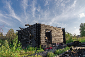 Burnt old log house in the village on a bright summer day against the blue sky. Close-up