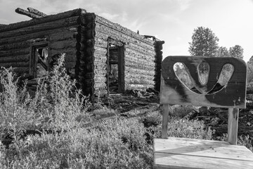 Burnt old log house in a village on a summer day against a gray sky. Black and white image. Close-up