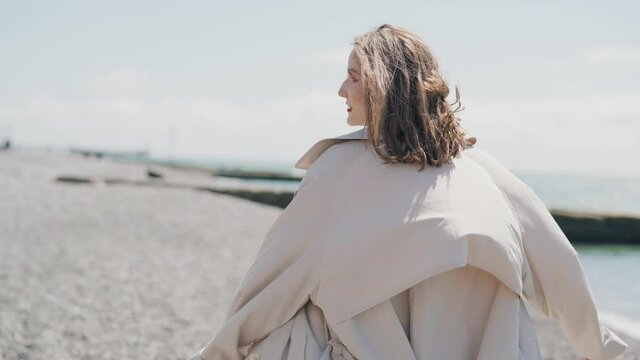 Young woman in trench coat walking on beach