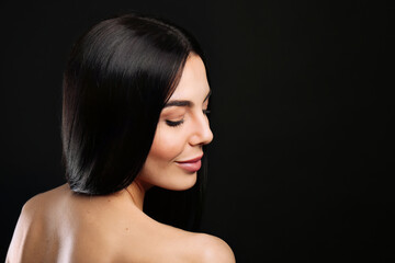 Fototapeta premium Portrait of happy young woman with beautiful black hair and charming smile on dark background, space for text