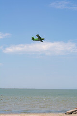 Fototapeta premium Old green retro plane flies in the blue sky over the sea on a summer day, background, place for text.